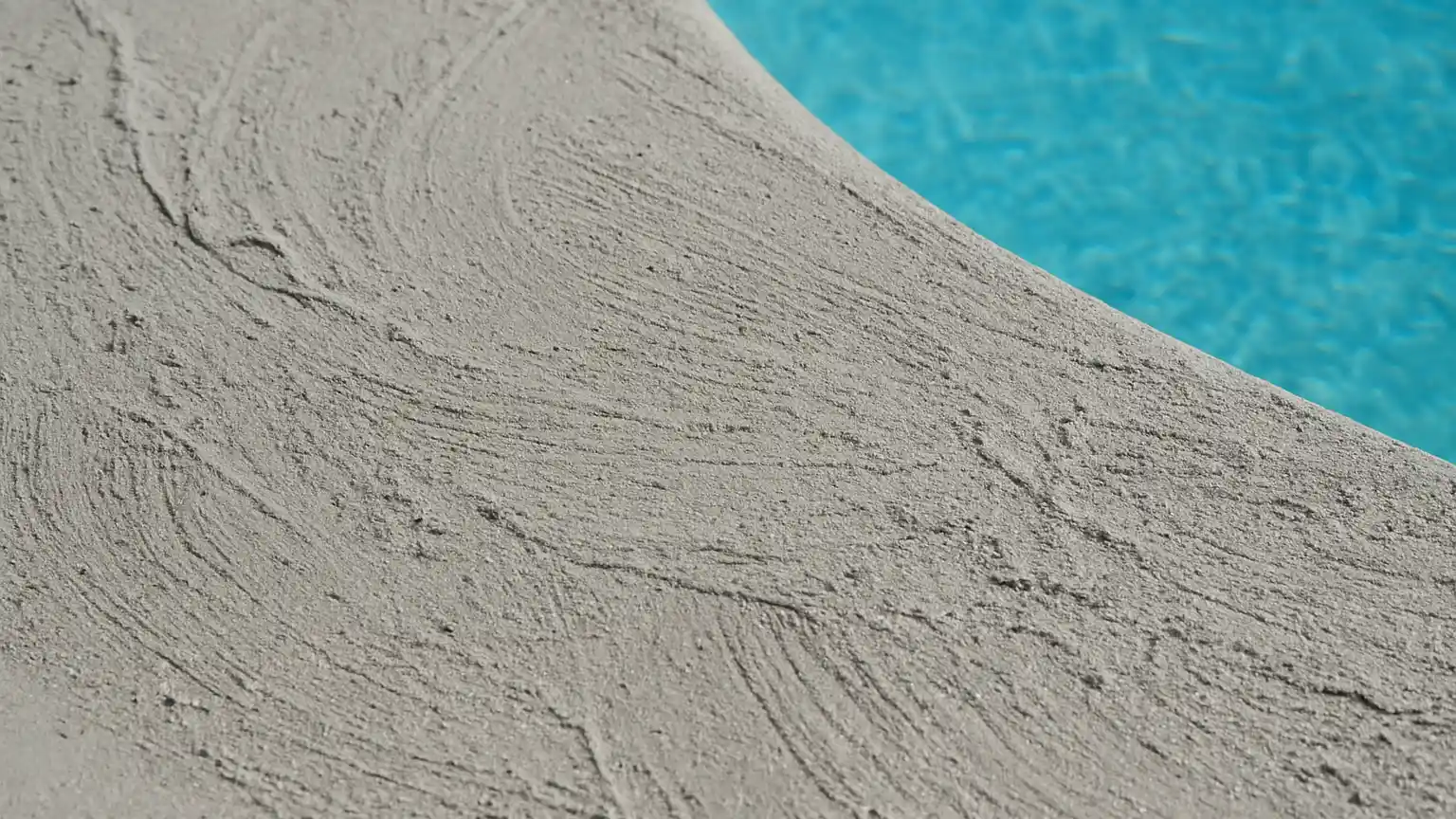 Close-up of new plaster pool surface with visible trowel marks, fine dust particles, and wet cement texture still curing, water line visible.